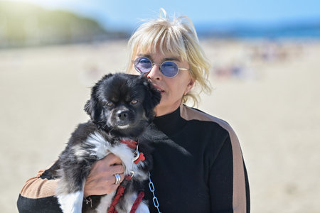 Retired mature blonde woman walking her dog alone on the beachの写真素材