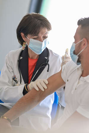 Injection of the vaccine against the virus by a female doctor in his medical officeの写真素材