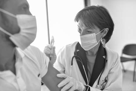 Injection of the vaccine against the virus by a female doctor in his medical officeの写真素材