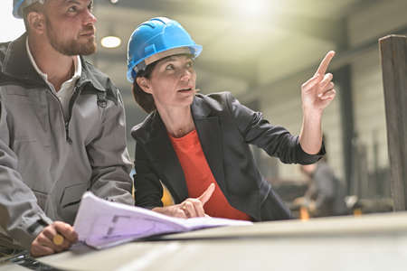 Confident female engineer is showing a blueprint to a male workerの写真素材