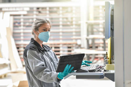 Woman engineer operating on a industrial digital machine and wearing protective mask against virusの写真素材