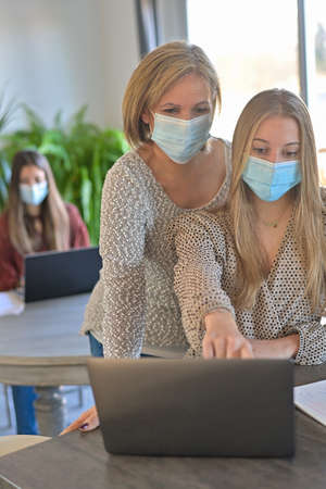 Students and their teacher wearing protective mask and working a lesson on a laptop at home during lockdown due to pandemicの写真素材