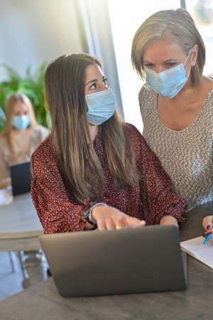 Twin sisters and their mother wearing protective mask and working a lesson on a laptop at home during lockdown due to pandemicの写真素材