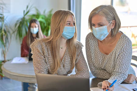 Twin sisters and their teacher wearing protective mask and working a lesson on a laptop at home during lockdown due to pandemicの写真素材