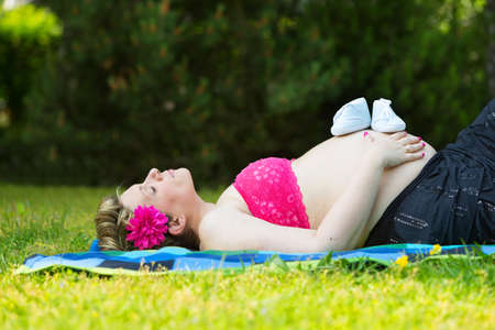 Pregnant woman lying in green grass with baby shoesの写真素材