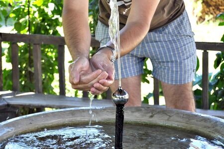 Young man putting hands under spouting waterの写真素材