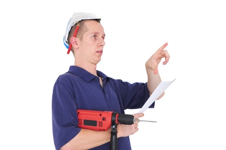 Young serious man with drill, blueprints and paper hat pointingの写真素材