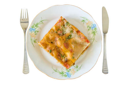 Lasagna slice in a plate with fork and knife isolated on whiteの写真素材