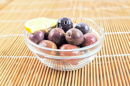 Fresh black olives and lemon slice in a glass bowlの写真素材