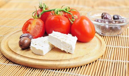 Fresh tomatoes, olives and white cheese on wooden boardの写真素材