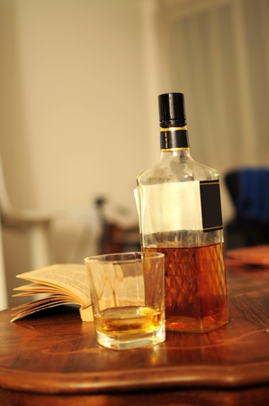 Glass of whiskey, bottle and opened book on home tableの写真素材