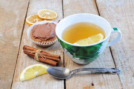 Tea, cupcake, cinnamon sticks and lemon slice on wooden backgroundの写真素材