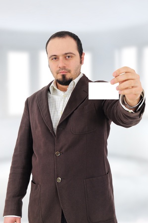 Young man in suit showing blank card, blurred interior backgroundの写真素材