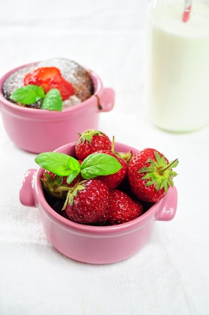 Fresh strawberries in a pink bowl, muffin and milk in the backgroundの写真素材