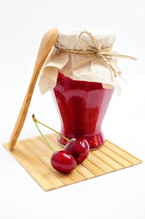 Jar of homemade cherry jam and couple of cherries with wooden spoon and coasterの写真素材