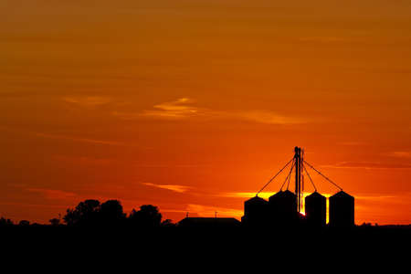 A silhouette of Midwestern grain bins against a beautiful setting sunの写真素材