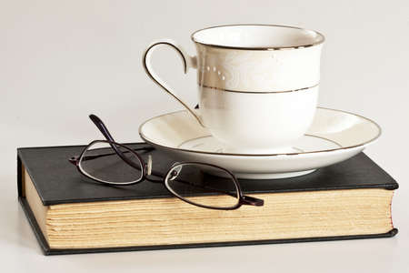 A cup of tea and glasses sit atop a black book.  の写真素材