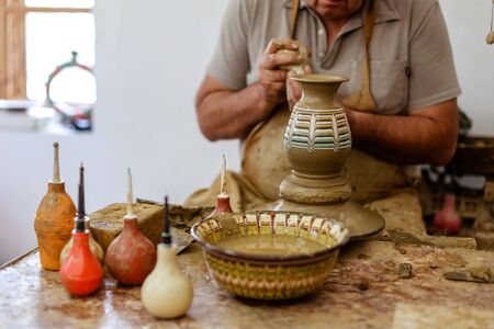 A Potter makes a jug with his hands a vase made of brown clay on a Potter's wheel in a traditional Bulgarian patternの写真素材