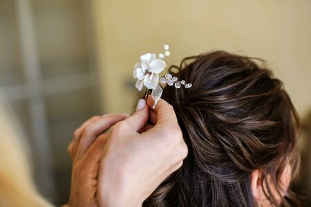 Close-up of a hairdresser stylist doing a girl's hair on long dark hair, holding a white flower...