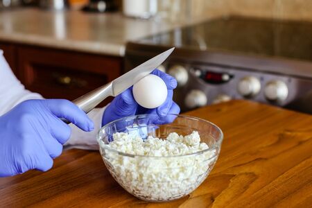 Close-up of hands in nitrile gloves breaking an egg with a knife.Cooking dough in the...