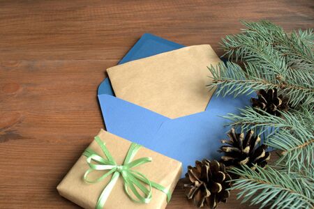 Christmas. On a brown wooden coat tree branch with cones and blue envelope. The envelope Christmas greetings. Near a box with a gift.の写真素材