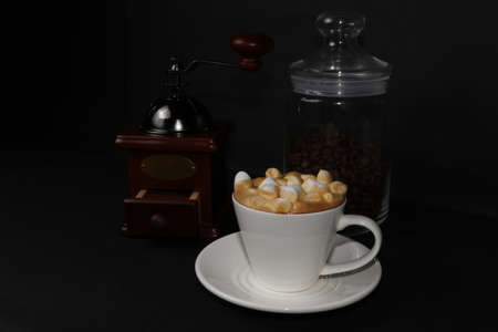 coffee grinder with coffee beans and a cup of coffee topped with sprinkled marshmallows, isolated on...