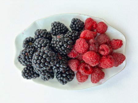 Large blackberries and raspberries on a small saucer isolated on a white background. Delicious and healthy berries for proper nutrition. Addition to an appetizing dessertの写真素材