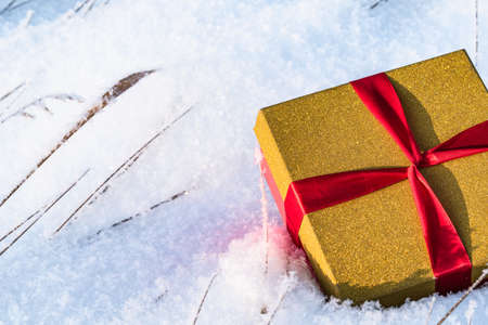 A gift box with a ribbon in the snow located on the right. Close-upの写真素材
