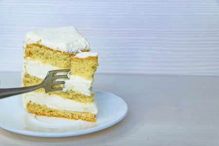 A fork pierces the vanilla buttercream cake on the left. White background.の写真素材