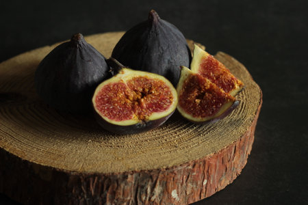 Whole and cut figs on a wooden stand on a black background