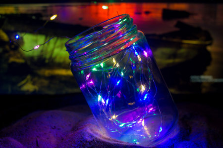 jar with little lights on the sand of a beach at sunsetの写真素材