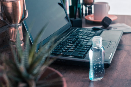 bottle of gel alcohol next to a laptop on a desk in a corner of the house as a home officeの写真素材
