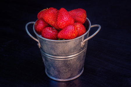 Fresh strawberries in a metal bucket on a black background. Selective focus.の写真素材