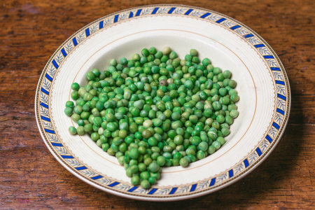 Green peas in a porcelain plate on a wooden table.の写真素材