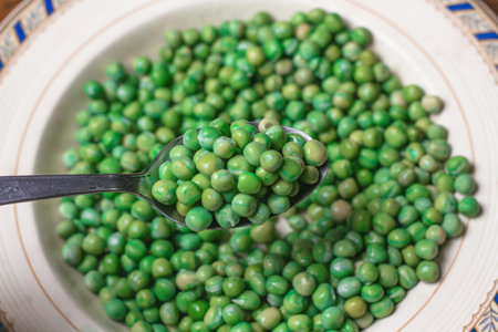 Green peas in a spoon on a white plate, close-upの写真素材