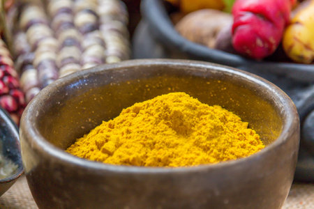 Turmeric powder in a wooden bowl and other spices in the backgroundの写真素材