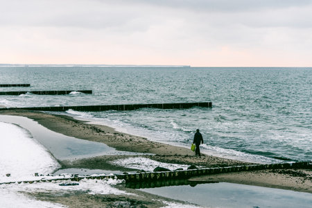 Seascape in winter with snow on the beach, waves breaking against wooden breakwatersの写真素材