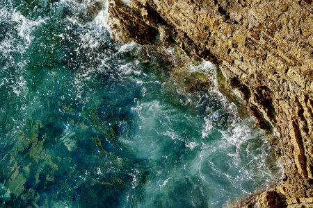 Seascape with turquoise ocean waves crashing against rocky coastal cliffs, aerial view
