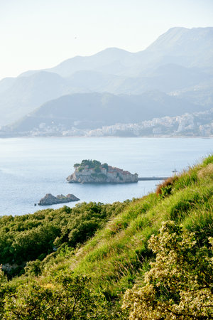 Scenic coastal landscape with a small island in the calm sea, surrounded by mountains and lush greeneryの写真素材