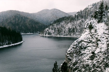 Landscape of a snow-covered mountain lake surrounded by forested cliffs in winter