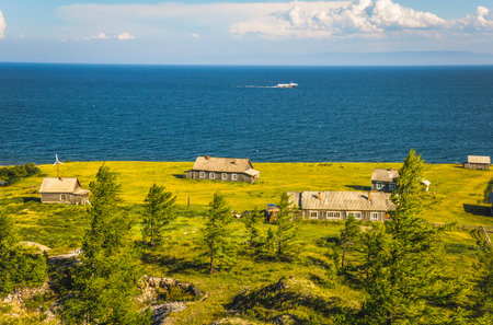 Coastal landscape with houses scattered on green hillside meadows overlooking deep blue ocean waters and cloudy skyの写真素材