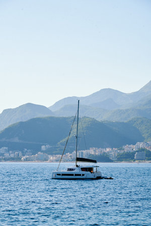 Seascape with a sailboat anchored in blue waters against a backdrop of coastal mountains