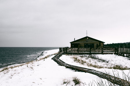 Small house on a snowy beach with wooden walkway along the coastの写真素材
