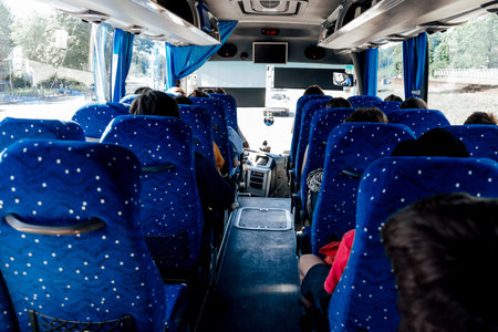 Interior view of a bus with blue patterned seats, showing the center aisle and passenger seating area during daytime travelの写真素材
