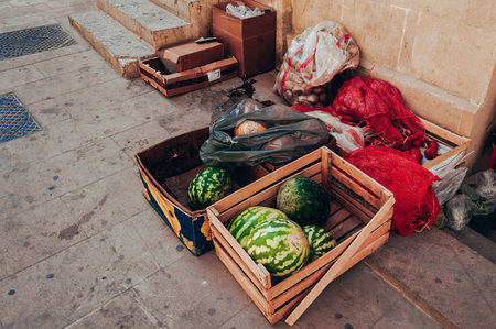 Wooden crates with watermelons and other produce displayed on the ground at a marketの写真素材