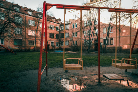 A swing set stands in the empty courtyard of a multi-storey building on a cloudy autumn day
