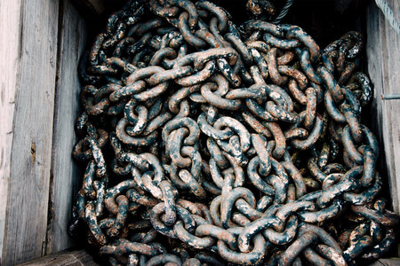 Large rusty metal chain from ship anchor lying in wooden box rebar texture