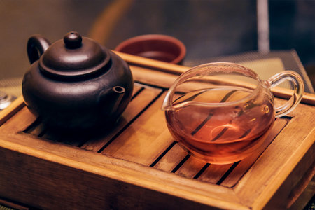 Fragrant healthy tea in a glass cup with a black clay teapot on a wooden serving trayの写真素材