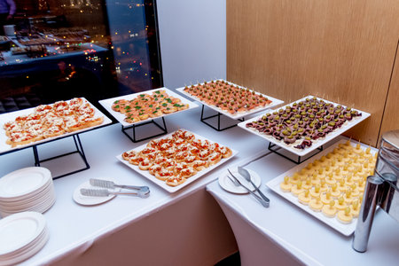 Buffet setup with various appetizers and tartlets arranged on white serving platters, displayed on a table with a white tableclothの写真素材