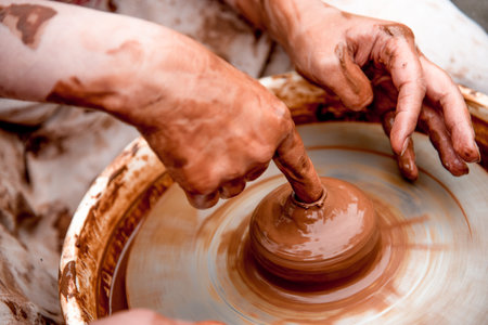 Potter sculpts a mug from clay, a close up of dirty hands creates a vase on a ceramist wheel